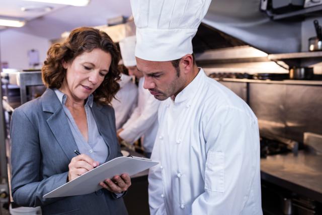 chef looks concerned at notes made by inspector